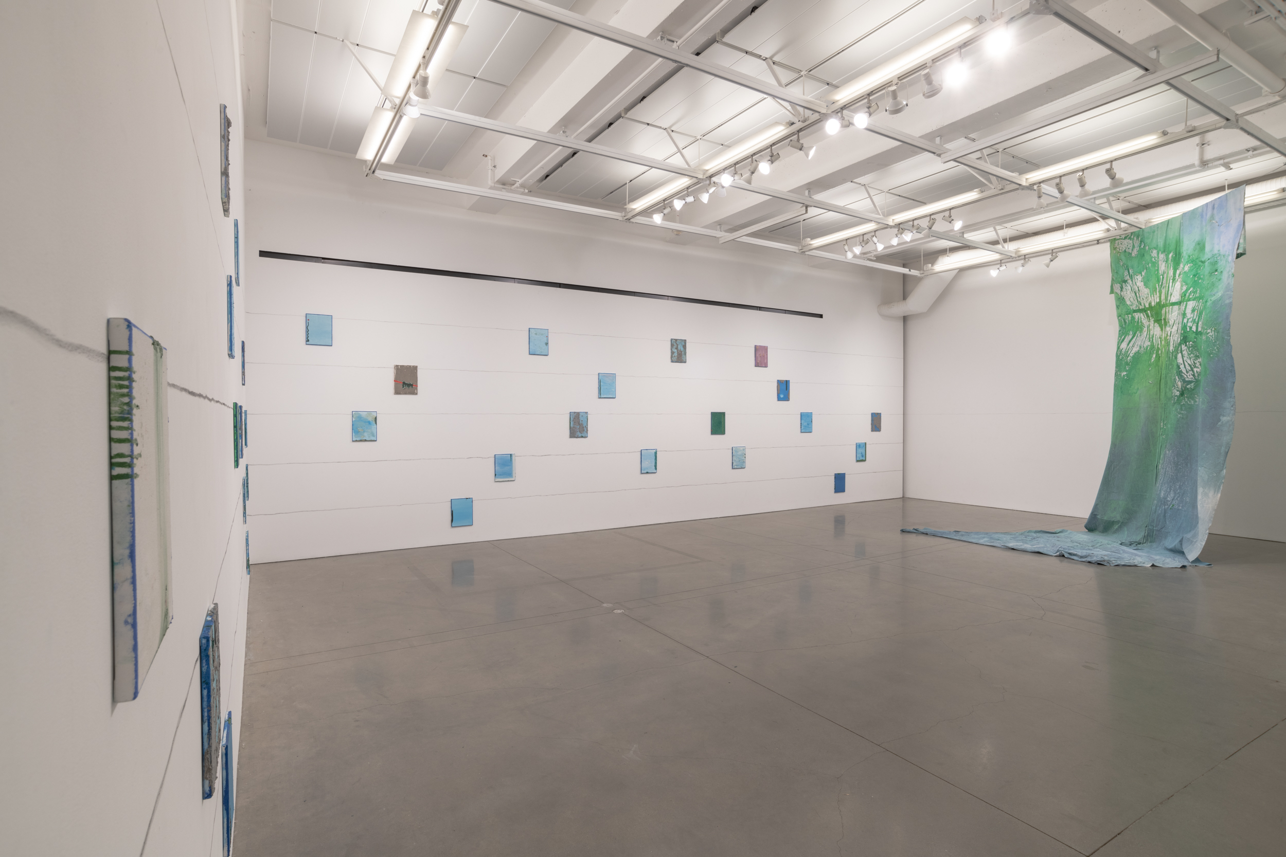 Installation views thesis exhibition containing colorful paintings stretched and unstretched, hanging in space and attached to the wall
