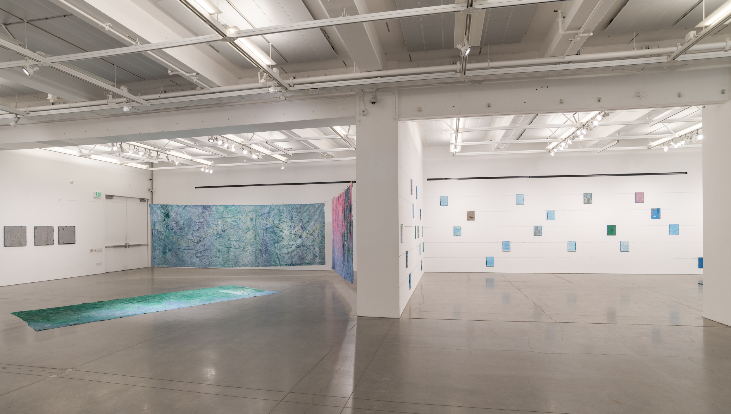 Installation views thesis exhibition containing colorful paintings stretched and unstretched, hanging in space and attached to the wall
