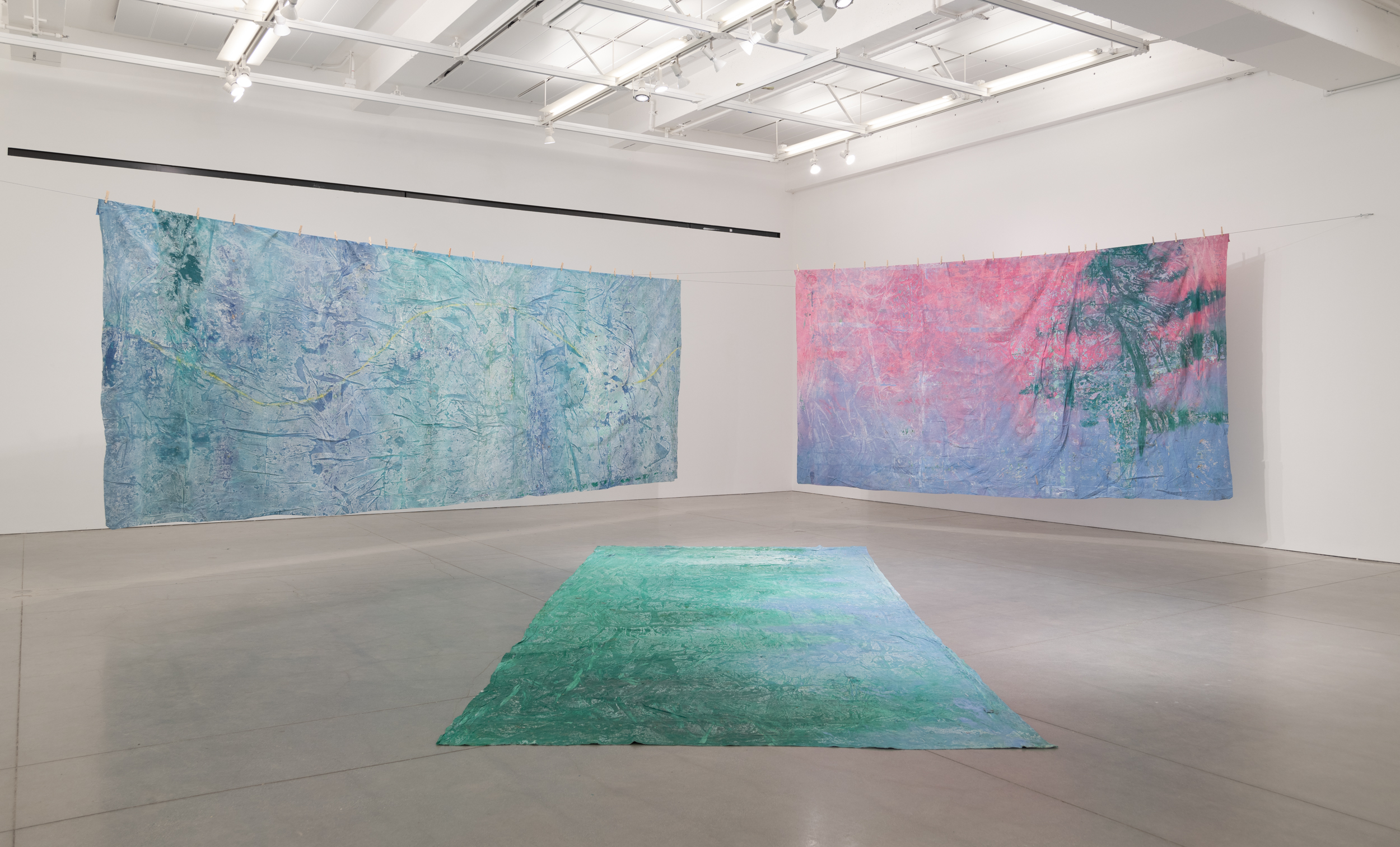 Installation views thesis exhibition containing colorful paintings stretched and unstretched, hanging in space and attached to the wall
