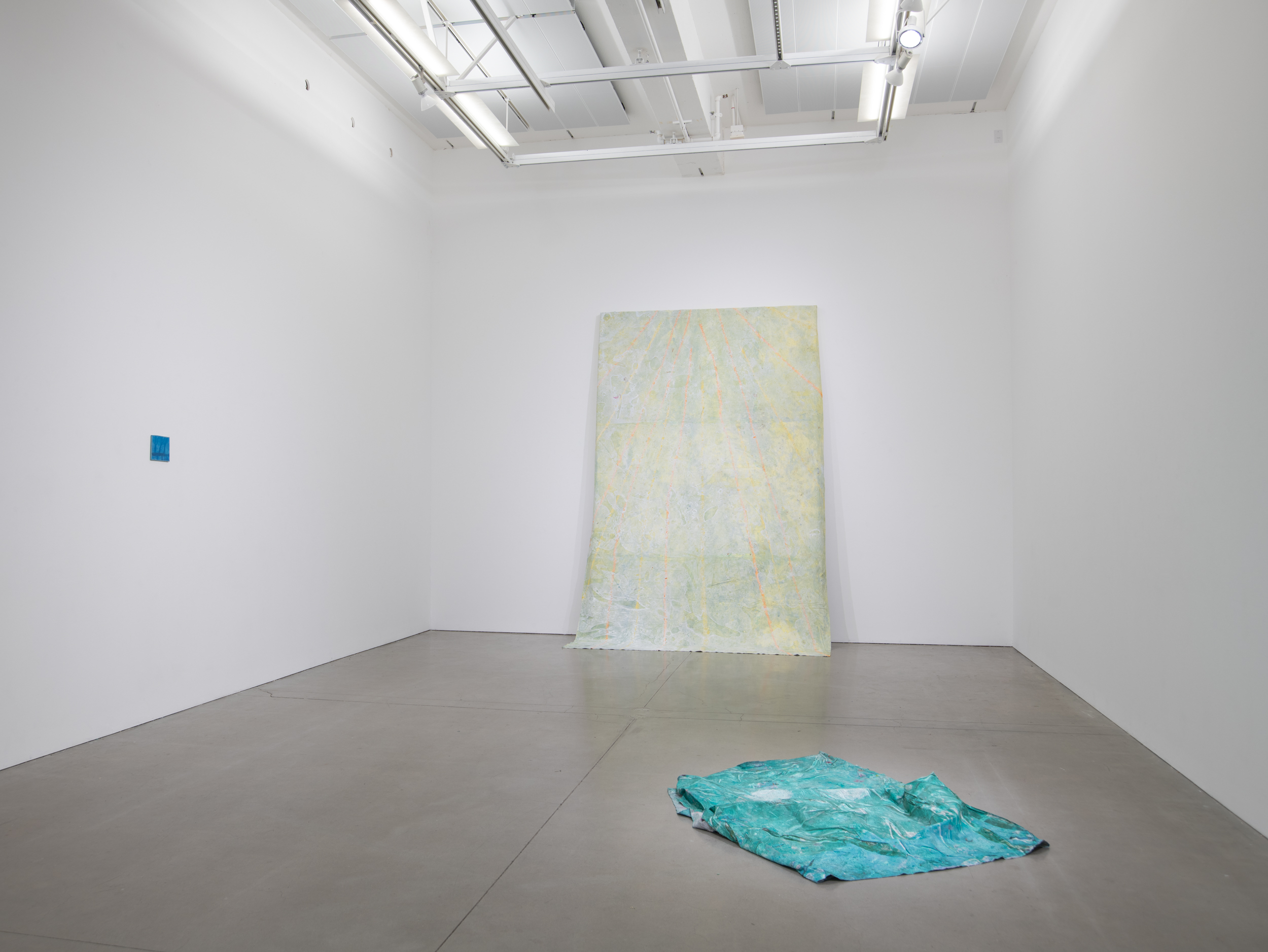 Installation views thesis exhibition containing colorful paintings stretched and unstretched, hanging in space and attached to the wall
