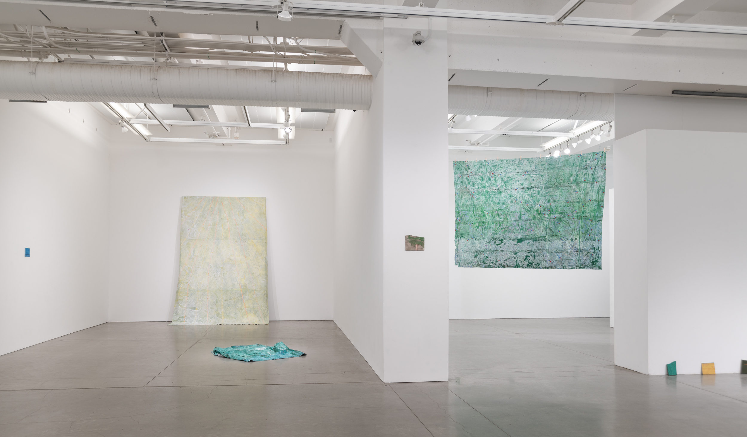 Installation views thesis exhibition containing colorful paintings stretched and unstretched, hanging in space and attached to the wall
