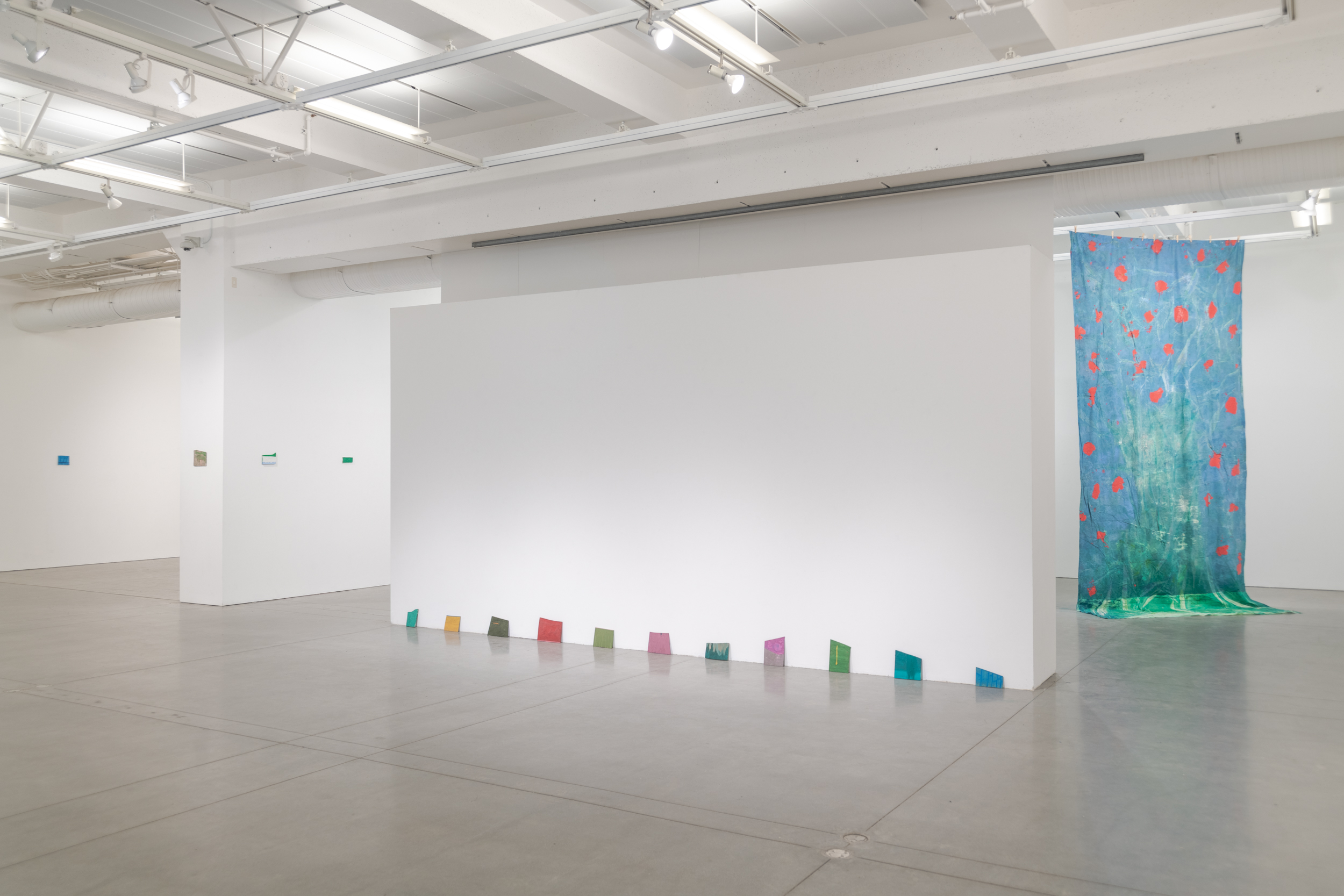 Installation views thesis exhibition containing colorful paintings stretched and unstretched, hanging in space and attached to the wall
