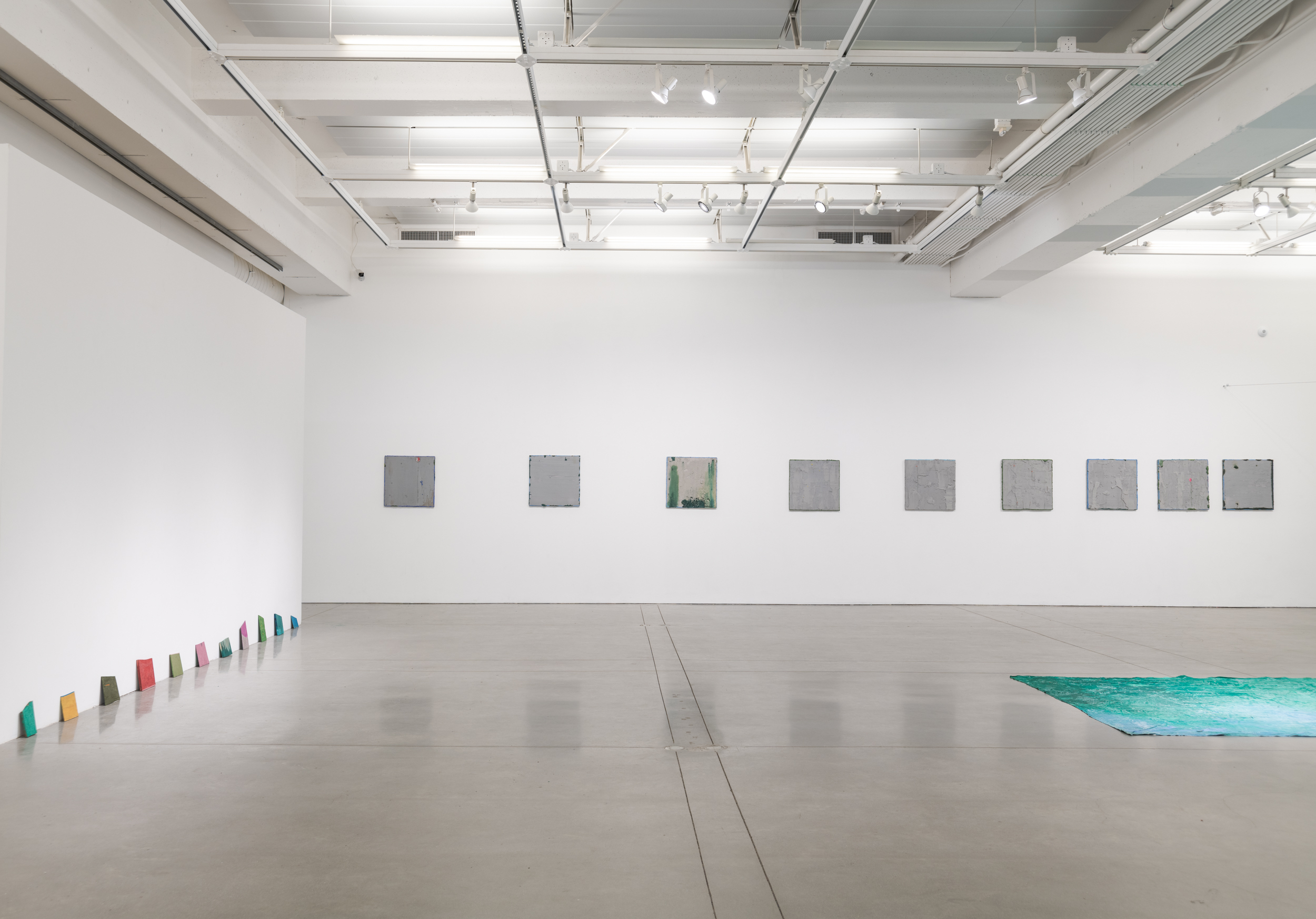 Installation views thesis exhibition containing colorful paintings stretched and unstretched, hanging in space and attached to the wall
