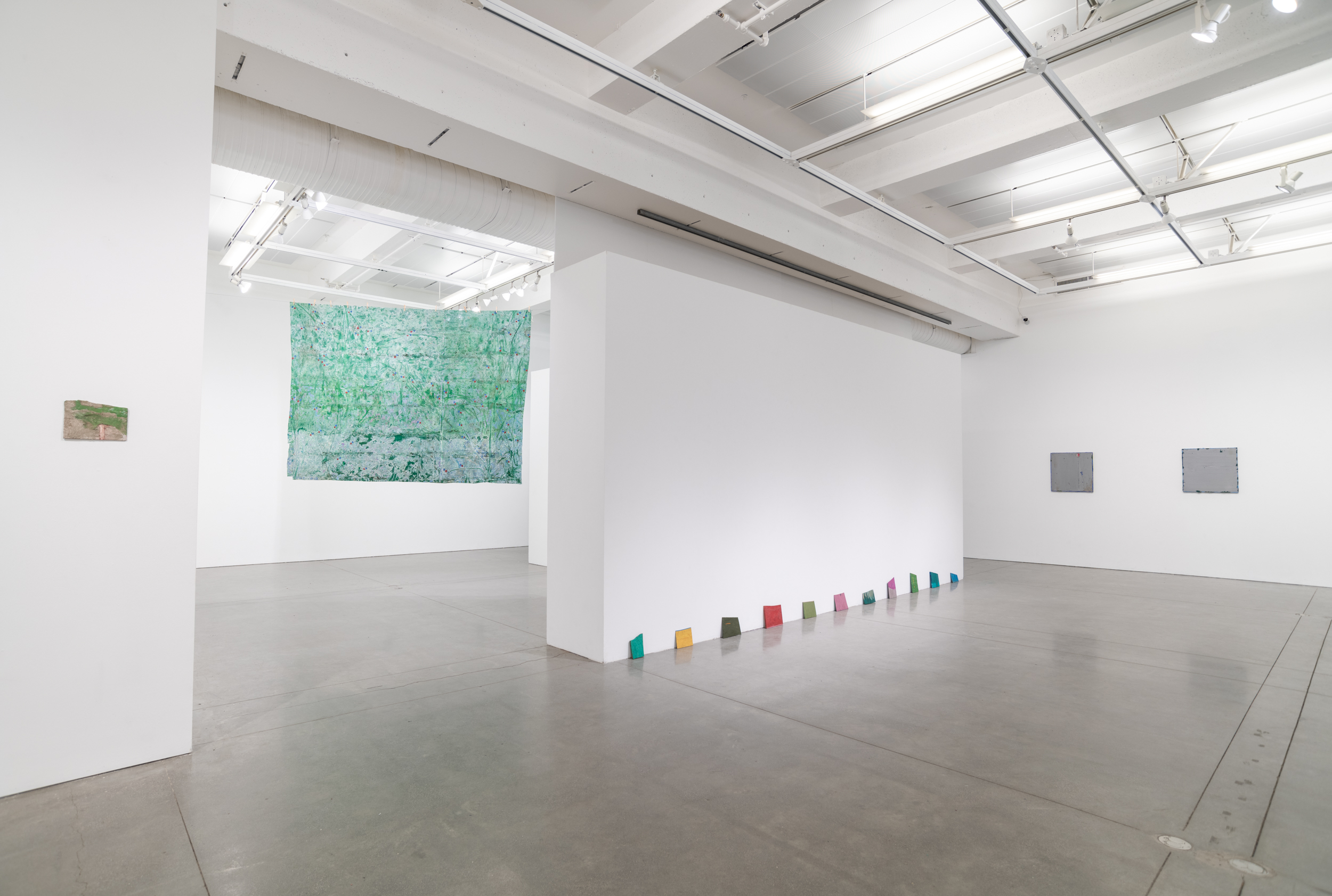 Installation views thesis exhibition containing colorful paintings stretched and unstretched, hanging in space and attached to the wall
