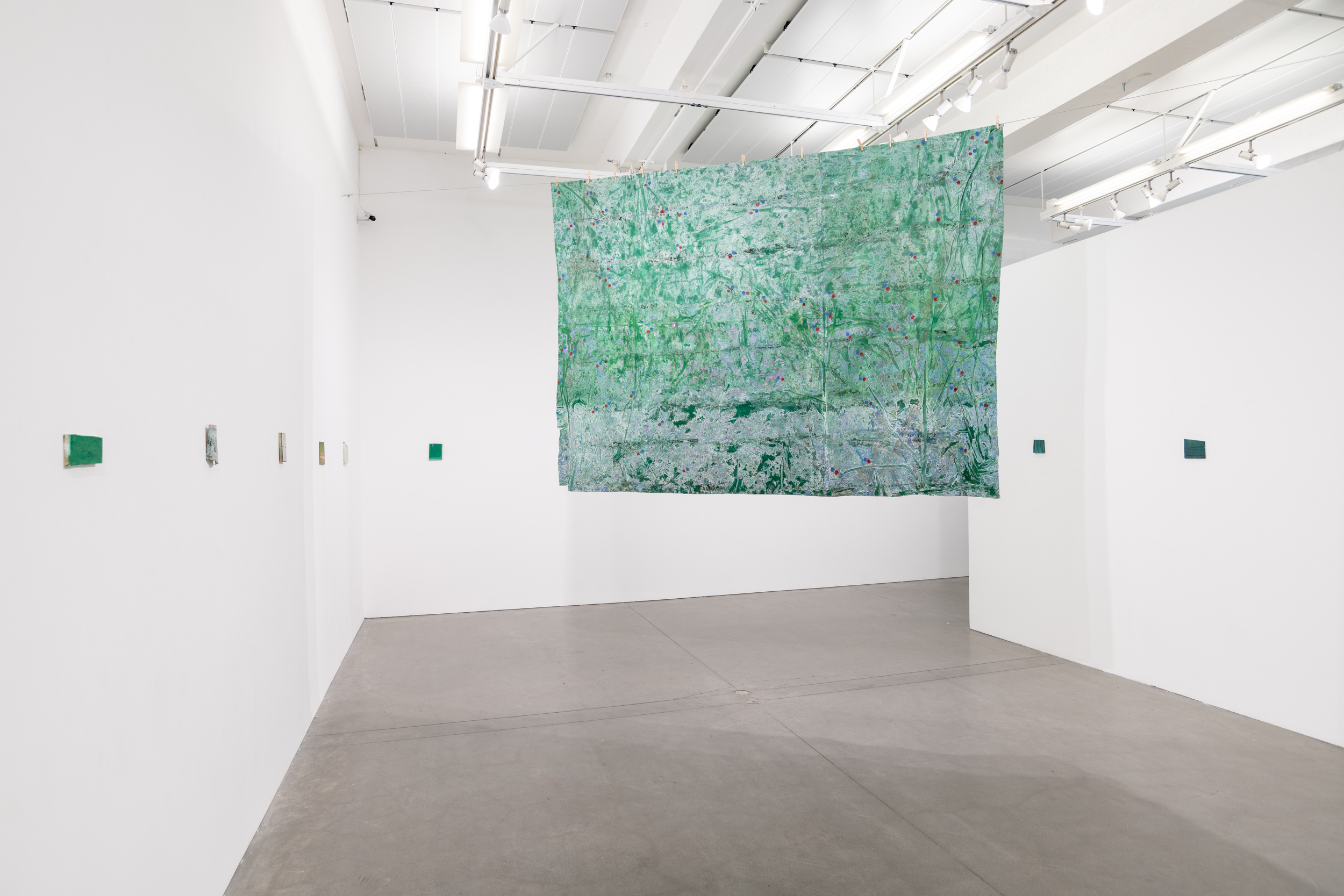 Installation views thesis exhibition containing colorful paintings stretched and unstretched, hanging in space and attached to the wall
