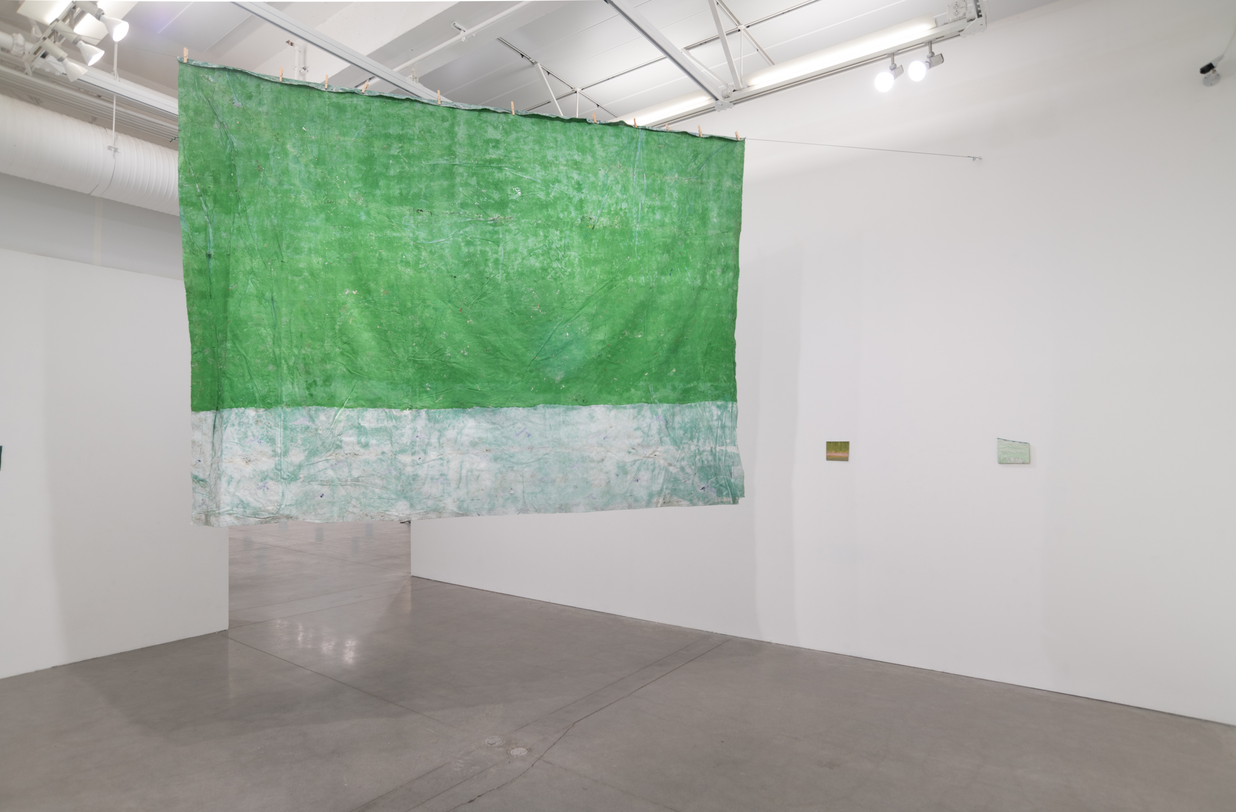 Installation views thesis exhibition containing colorful paintings stretched and unstretched, hanging in space and attached to the wall
