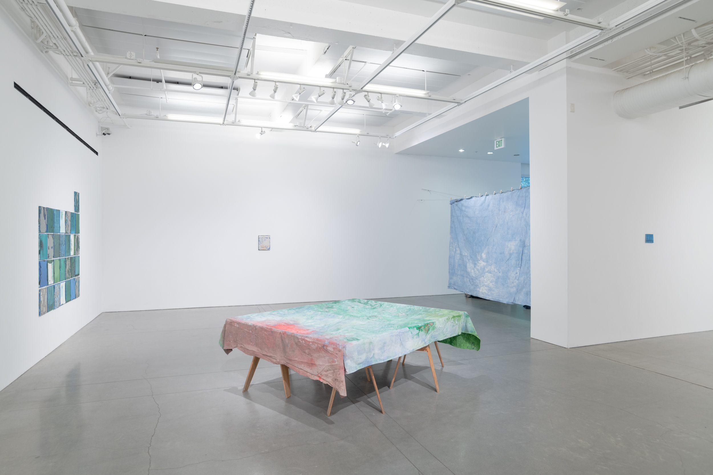 Installation views thesis exhibition containing colorful paintings stretched and unstretched, hanging in space and attached to the wall
