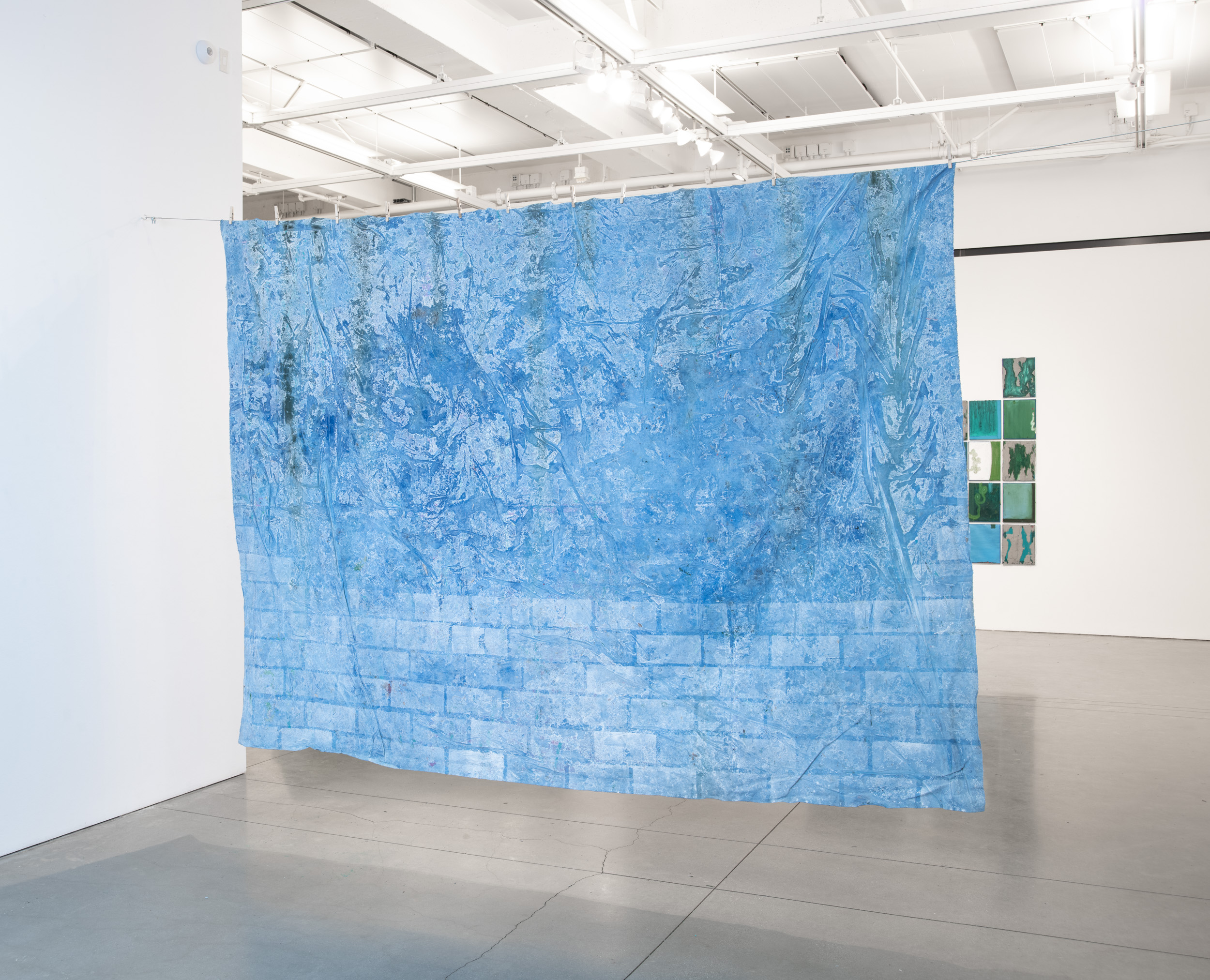 Installation views thesis exhibition containing colorful paintings stretched and unstretched, hanging in space and attached to the wall
