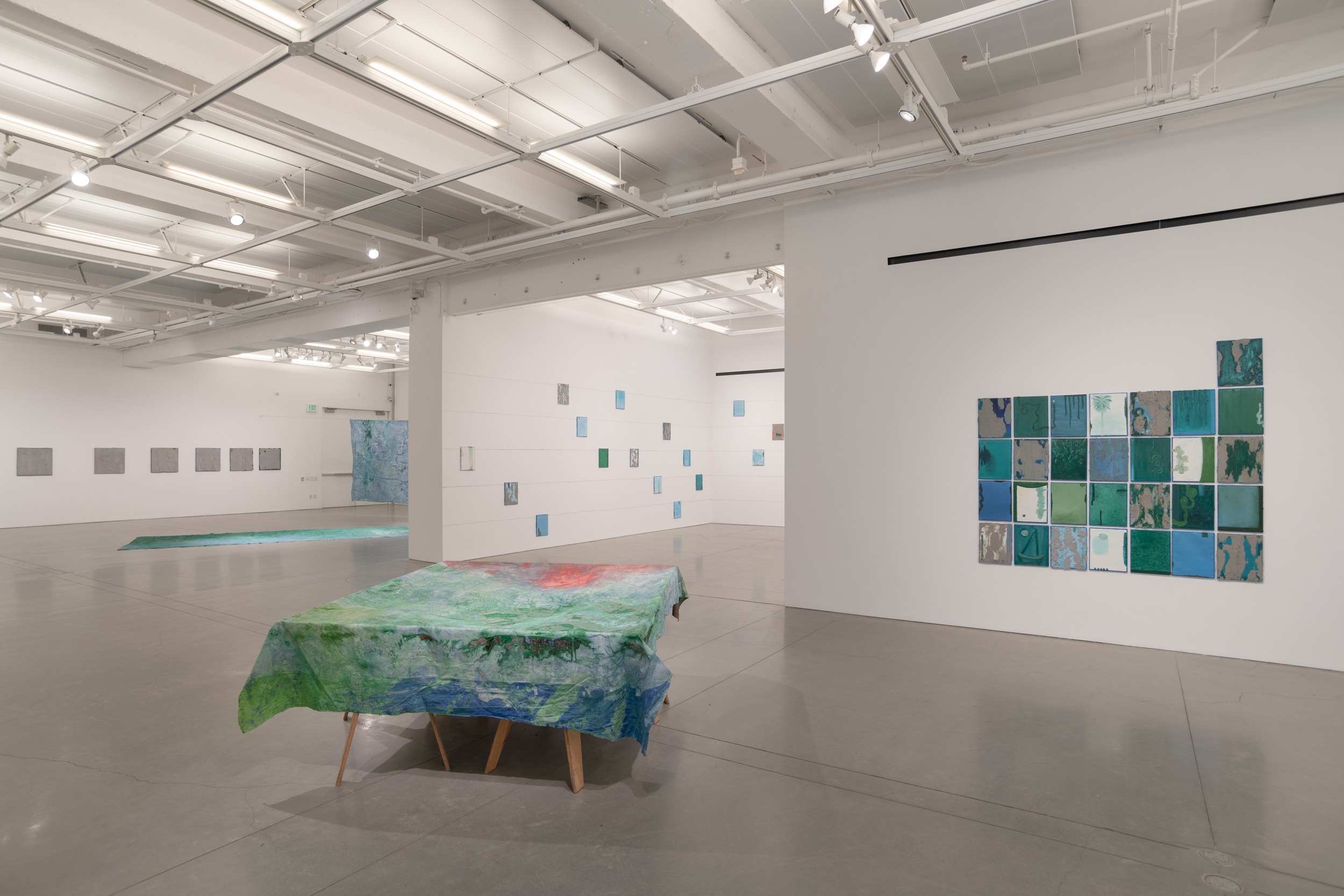 Installation views thesis exhibition containing colorful paintings stretched and unstretched, hanging in space and attached to the wall
