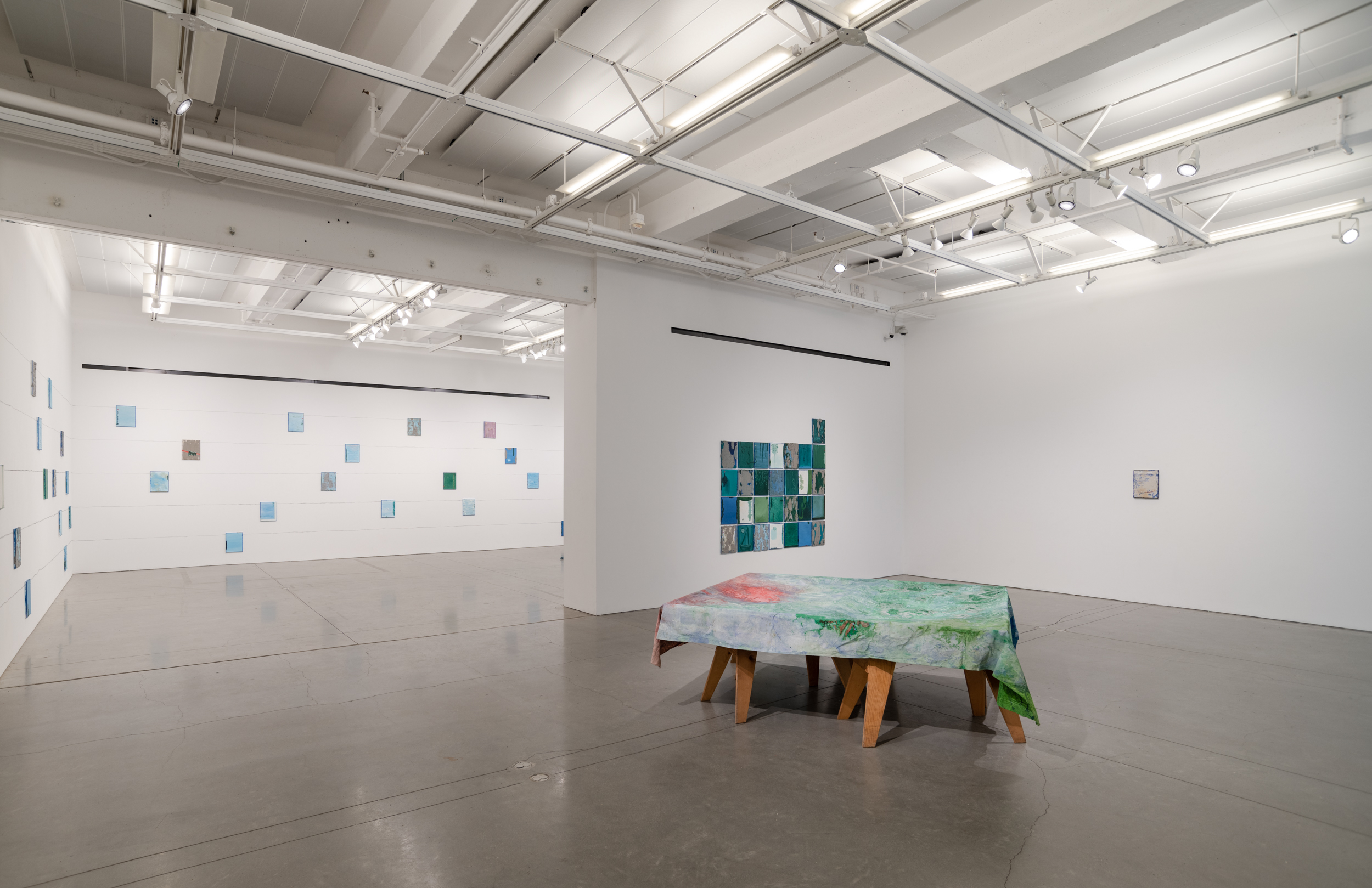 Installation views thesis exhibition containing colorful paintings stretched and unstretched, hanging in space and attached to the wall
