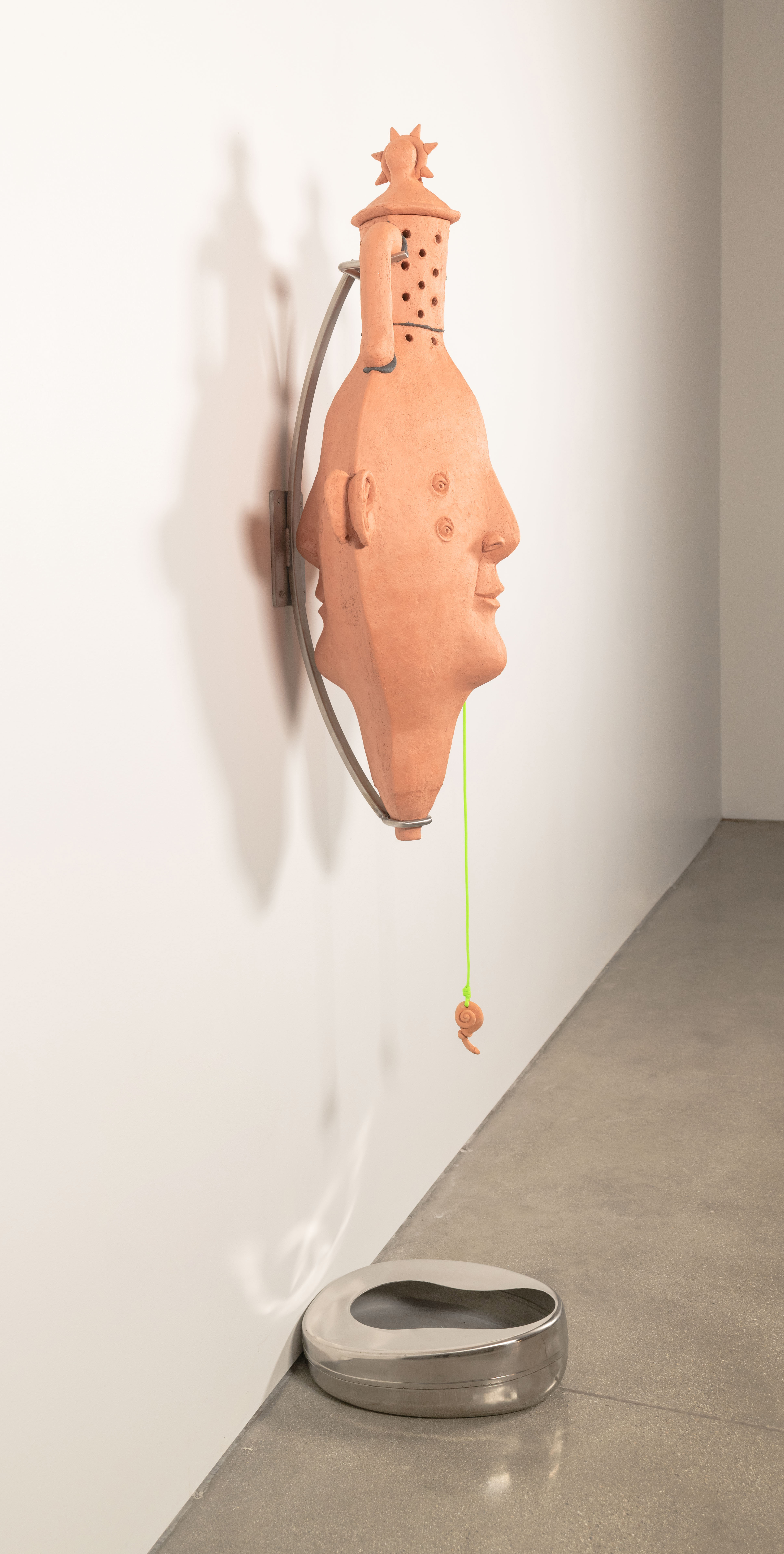 An anthropomorphic amphora hangs from the wall on a stainless steel mount
positioned over a bedpan. There is a lid and holes on the neck of the vase. Its base comes to a
point with a hole for drainage. From its ear hangs a snail-like charm on neon green Paracord.
Inside, red worms eat organic waste collected from my garden and the UCLA graduate studios.
Through the vermicomposting process a leachate is produced that collects in the bedpan
bellow.