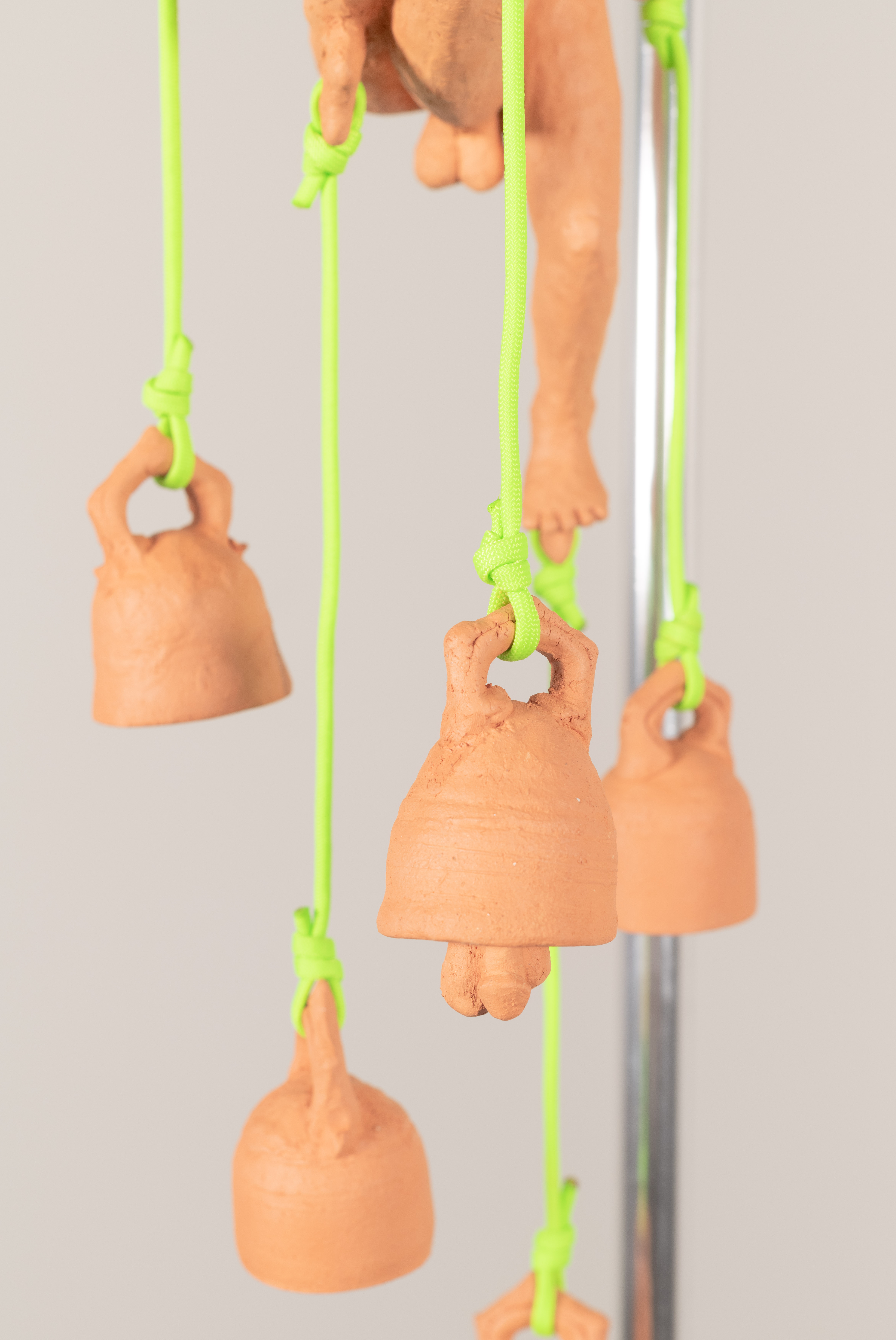 Detail of ceramic bells with phallic clappers that are attached by neon green Paracord. 