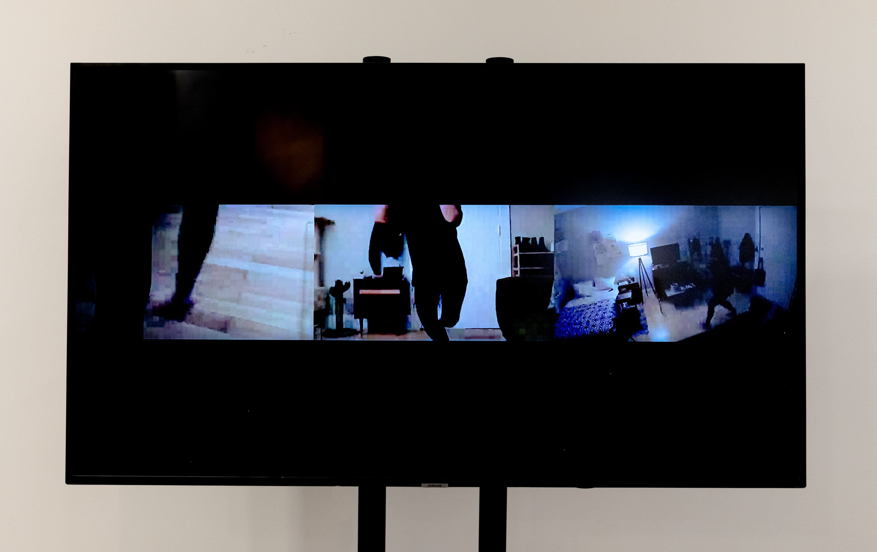 Channel on the left is focused on feet movement. Channel in  the middle is focused on the whole body with the camera in a head-on frontal position. The third channel is at a birds eye view and the camera is pointed from above and the viewer is able to see the artist’s apartment Channels turn on and off according to the rhythm of the music. The sound is the artist singing New York, New York by Frank Sinatra, but the sound comes in and out. It oscillates between silence and singing.
