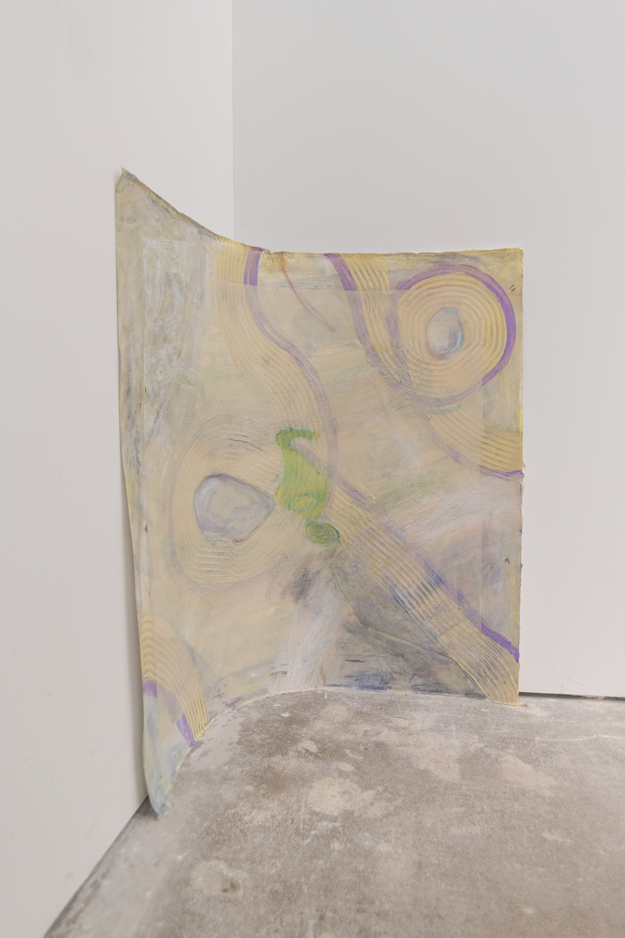 Paper is nestled into the corner of the room. It sits against the wall with half of it on one wall and the other half on the perpendicular wall. Three yellow squeegee swirls outlined with purple run across the surface. A cloudy milky white arc sits on the bottom and top left. There is a taped off border revealing the preliminary painting. The bound box in the middle is slightly obscured and muted with layers of cream paint. The center negative space is filled in with lime green and outlined by white oil pastel.
